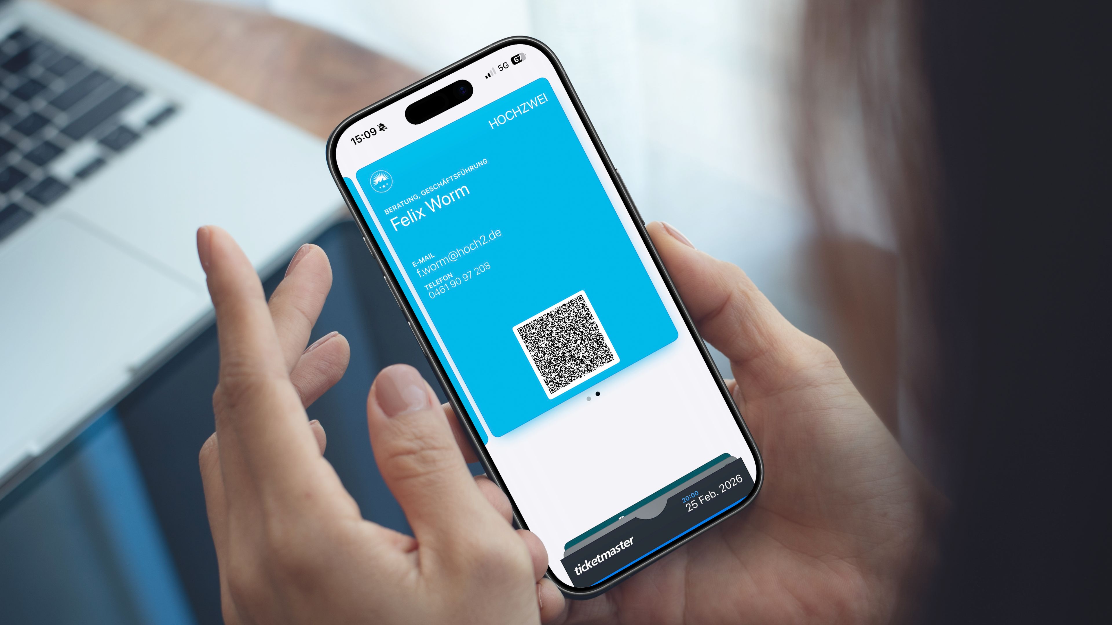 Eine Person hält ein Smartphone mit einer digitalen Visitenkarte mit Name, E-Mail-Adresse, Telefonnummer und einem QR-Code