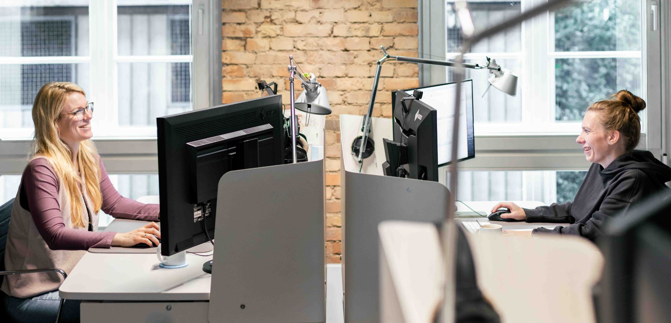Zwei Mitarbeiterinnen von Hochzwei an ihren gegenüberliegenden Arbeitsplätzen.