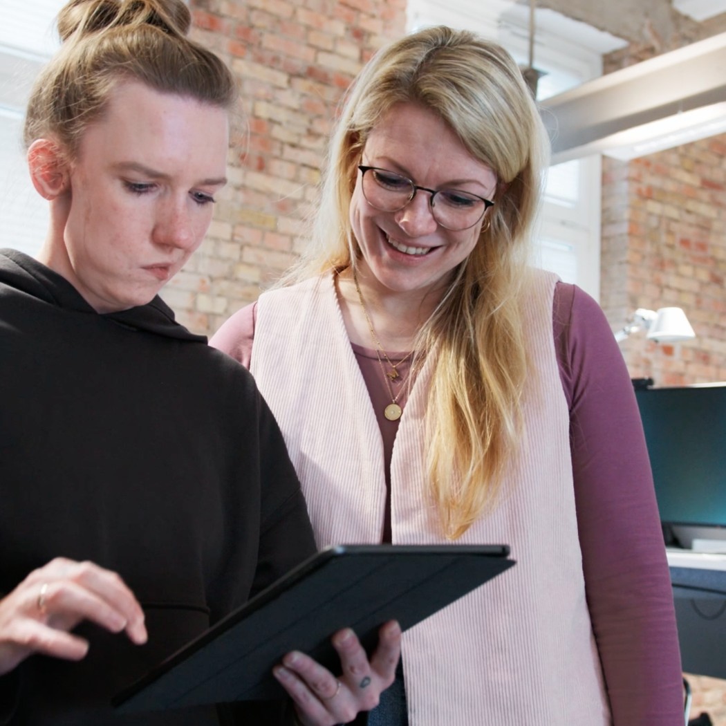 Zwei Kolleginnen von Hochzwei schauen sich gemeinsam etwas auf einem Tablet an
