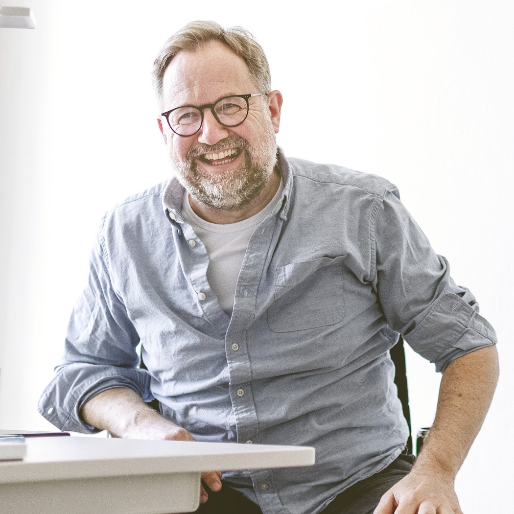 h2_einblicke_remote-onsite_teaser_01.jpg Der Standortleiter und Prokurist Björn Ihloff sitzt strahlend an seinem Arbeitsplatz.