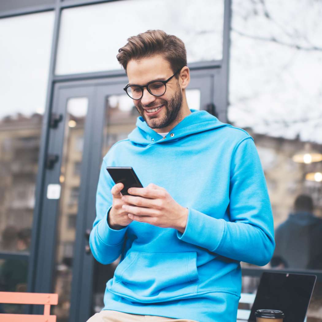 Ein junger Mann steht vor einem Gebäude mit dem Handy in der Hand