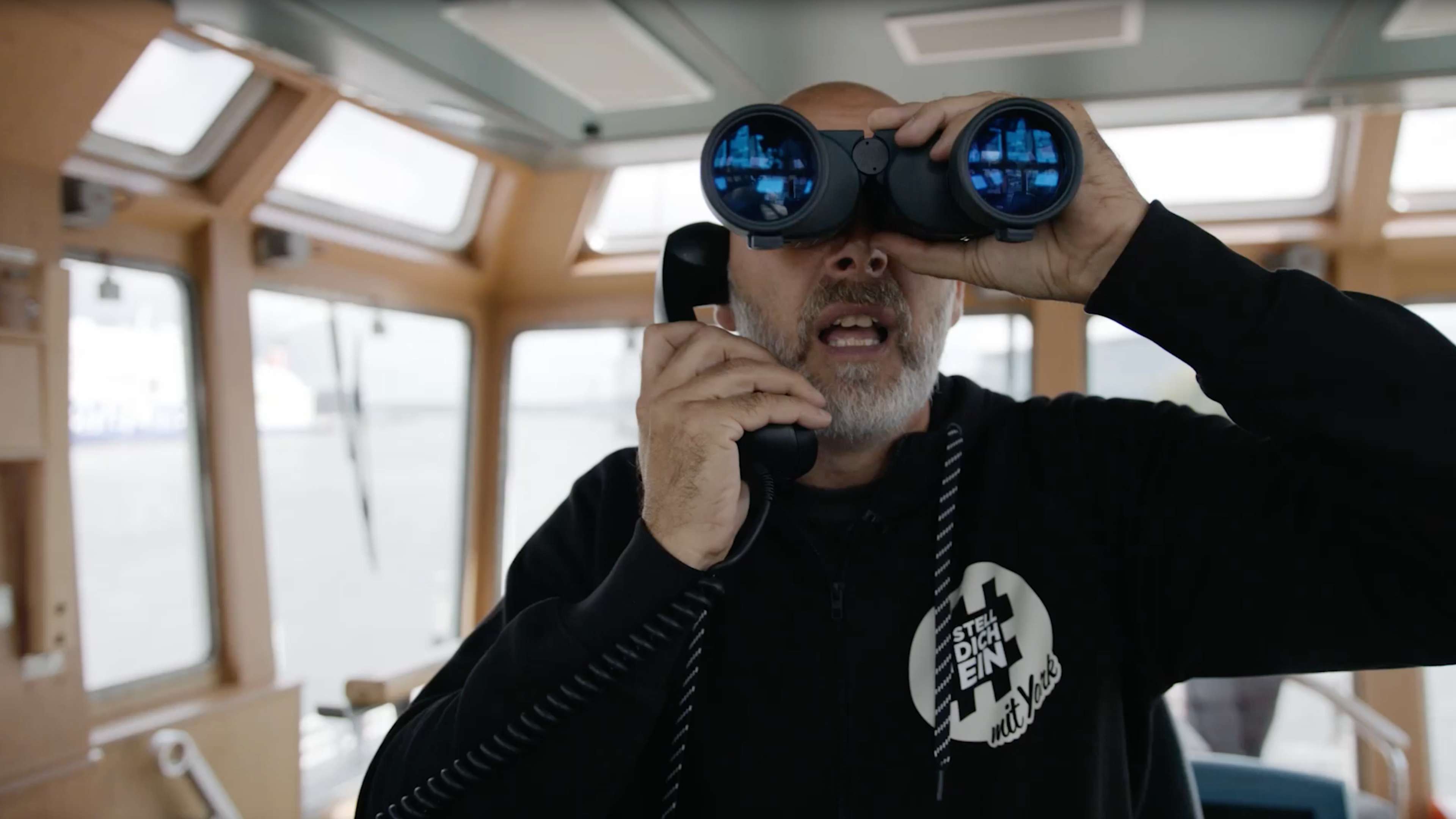 York in einem Schiff mit Fernglas und Telefonhörer in den Händen.