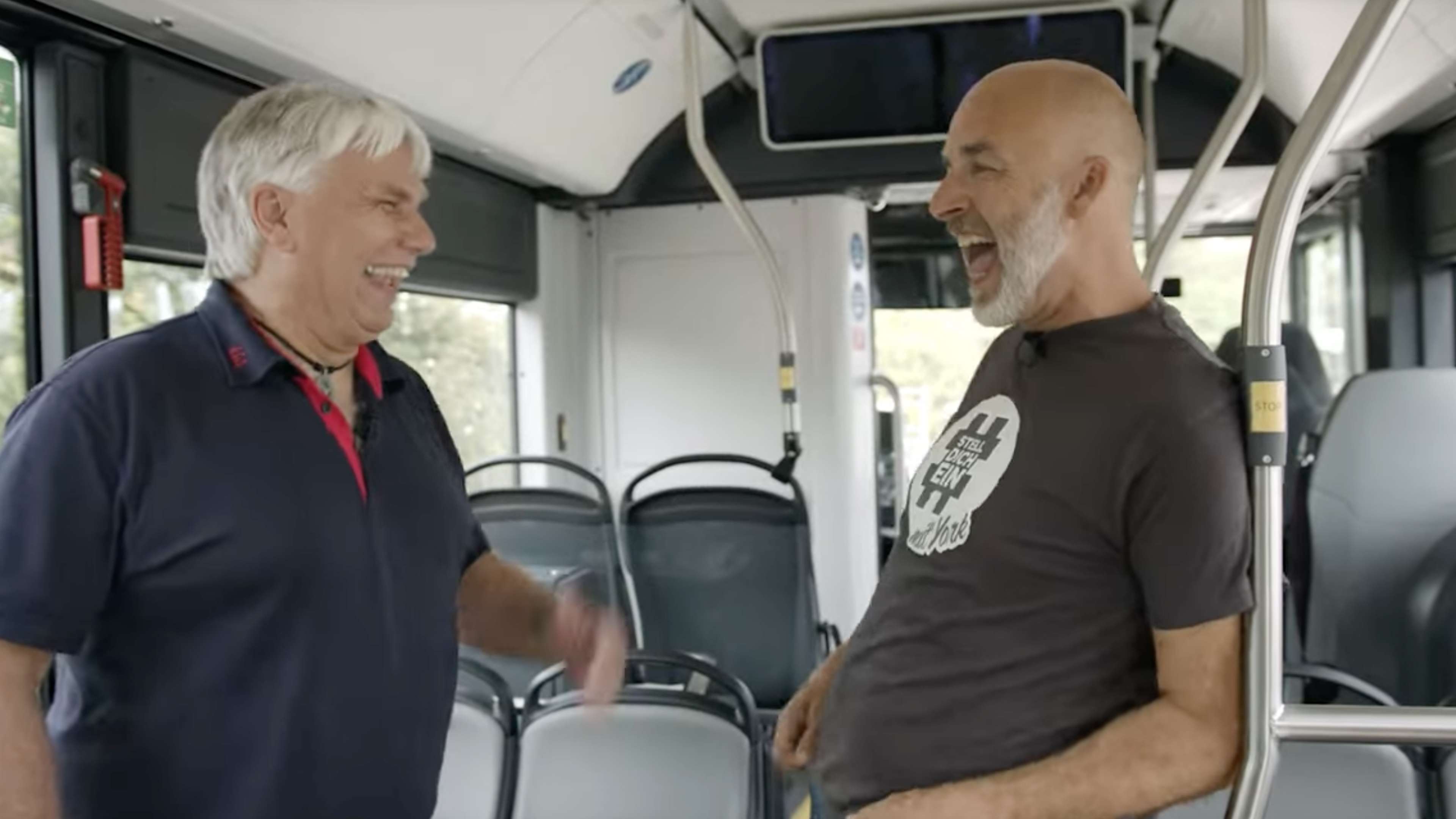 York lacht mit einem Busfahrer in einem leeren Linienbus.