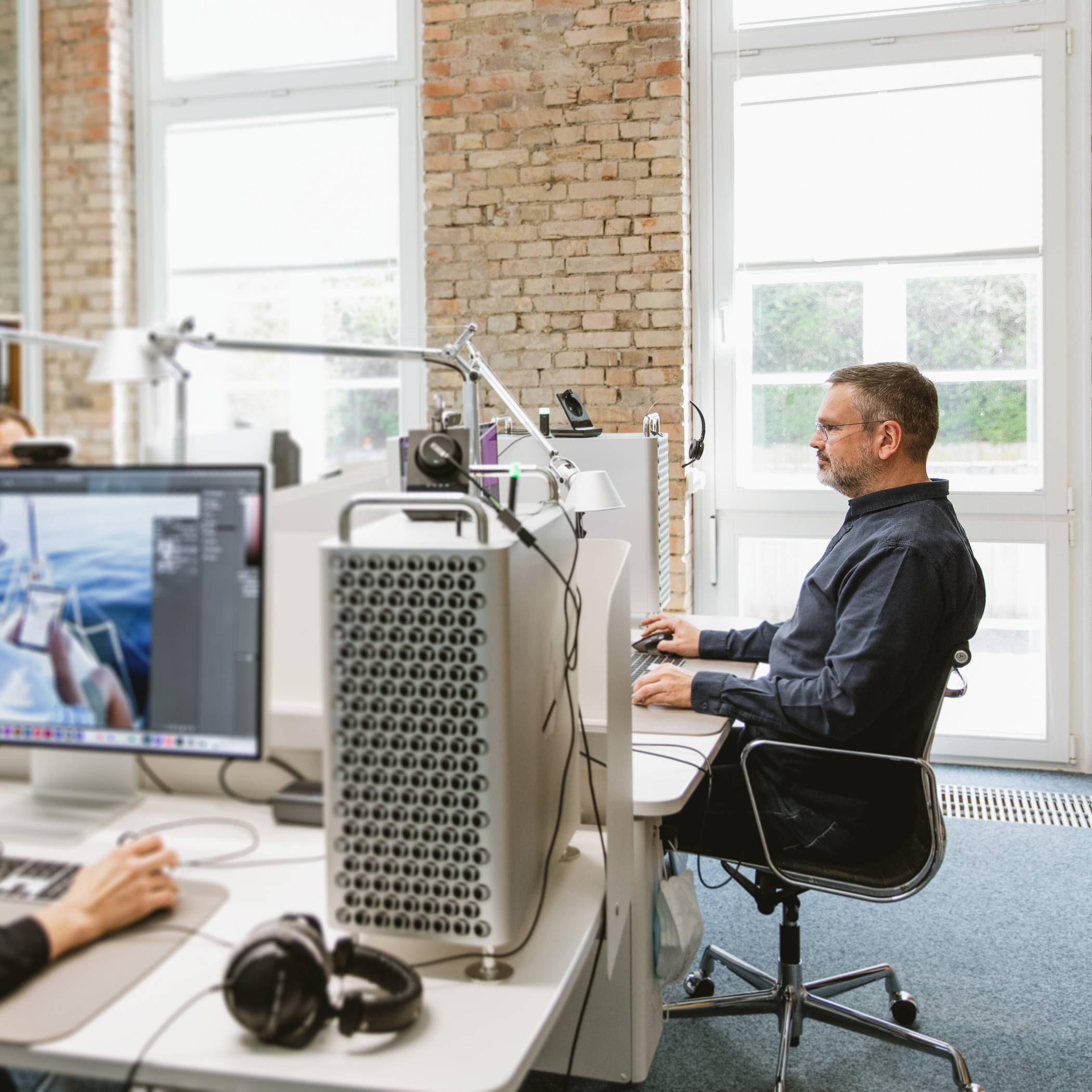 Seitlicher Blick auf einen am Schreibtisch sitzenden Mitarbeiter, links sind zwei weitere Arbeitsplätze erkennbar