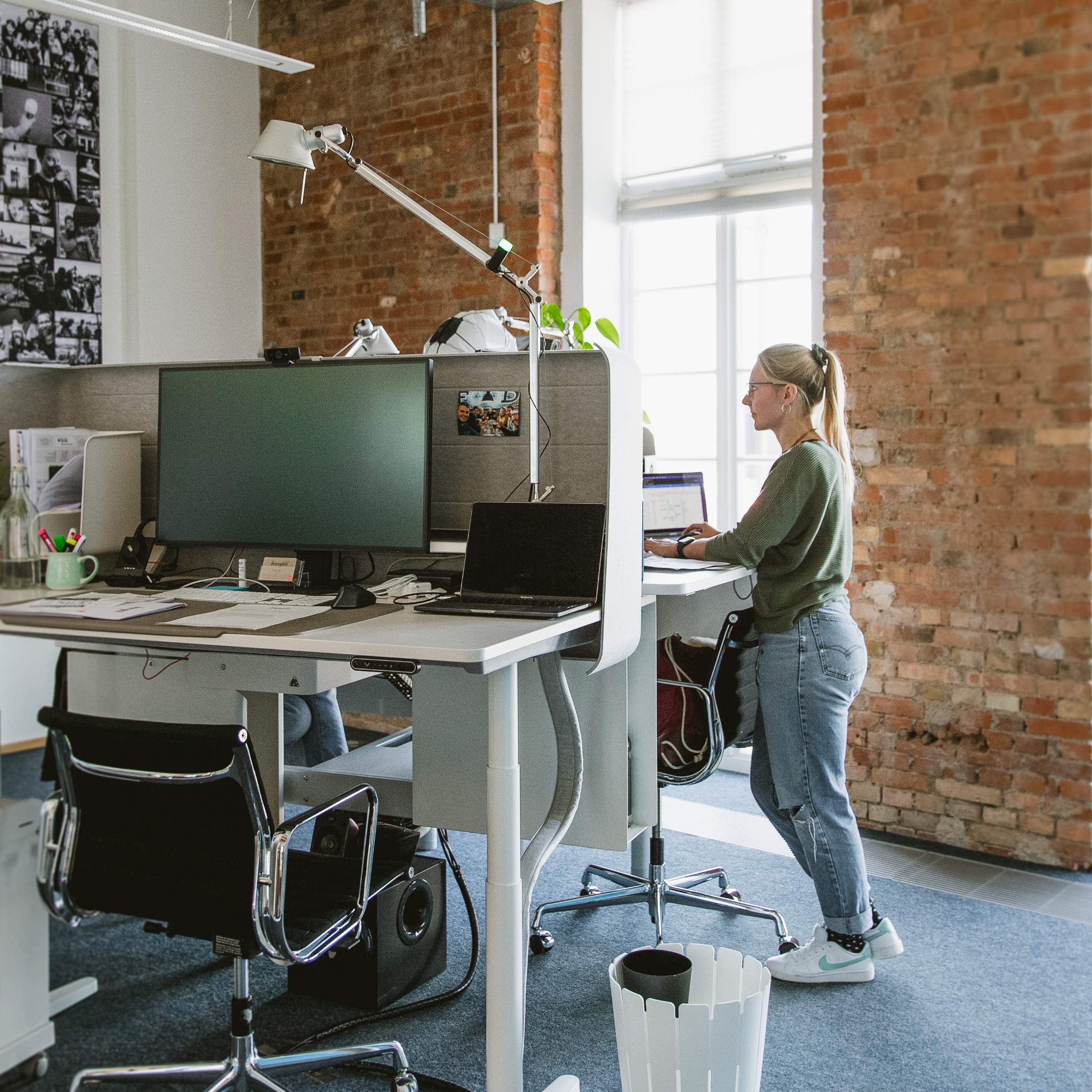 Eine Mitarbeiterin steht am höhenverstellbaren Schreibtisch, ein Arbeitsplatz ist leer