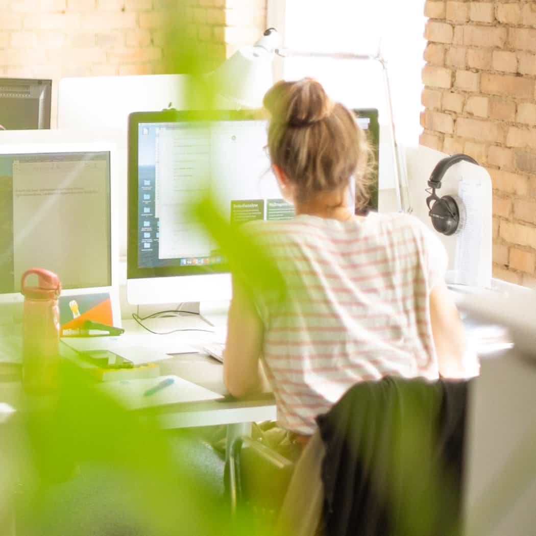 hochzwei_wir_teaser_08.jpg Blick von hinten in´s Büro auf Mitarbeiterin am Computer