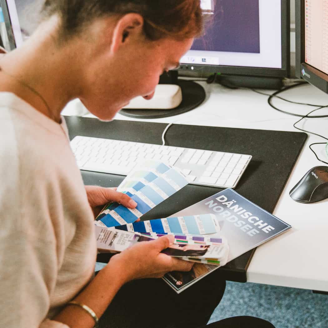 hochzwei_wir_teaser_09.jpg Mitarbeiterin vergleicht Farben auf einem Farbfächer
