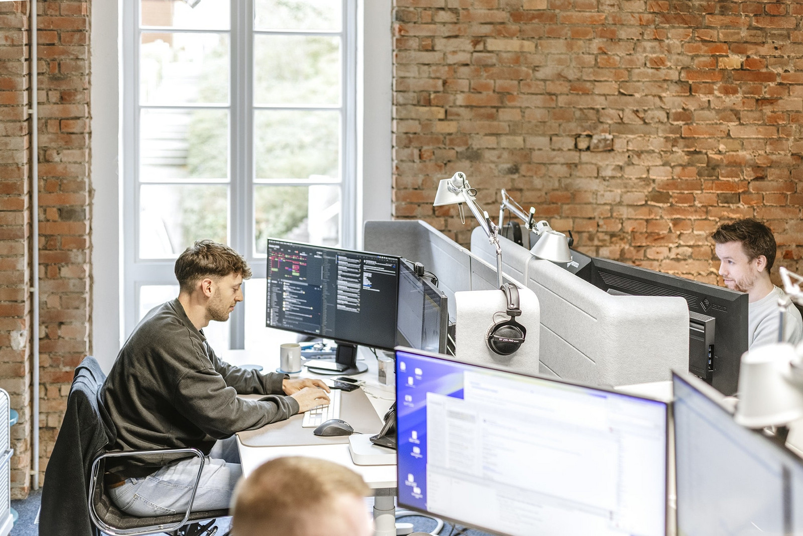 Blick auf drei Arbeitsplätze mit männlichen Mitarbeitern bei HOCHZWEI