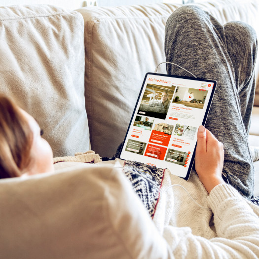 hochzwei_nospa_teaser_14.jpg Frau liegt auf dem Sofa und schaut sich die Nospa Homepage an