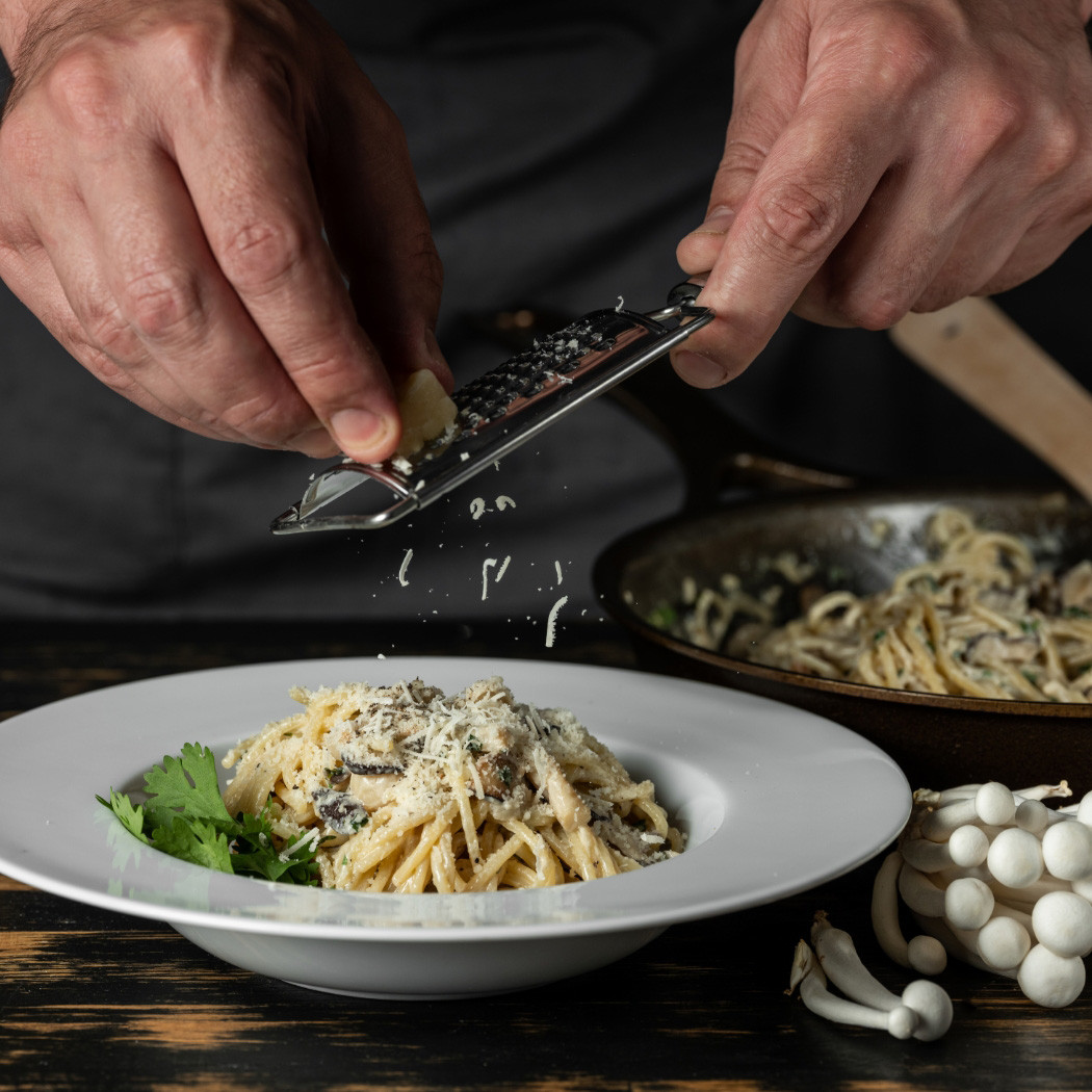 hochzwei_odore_teaser_01.jpg Hände, die Parmesan auf Spaghettigericht mit Reibe hobeln