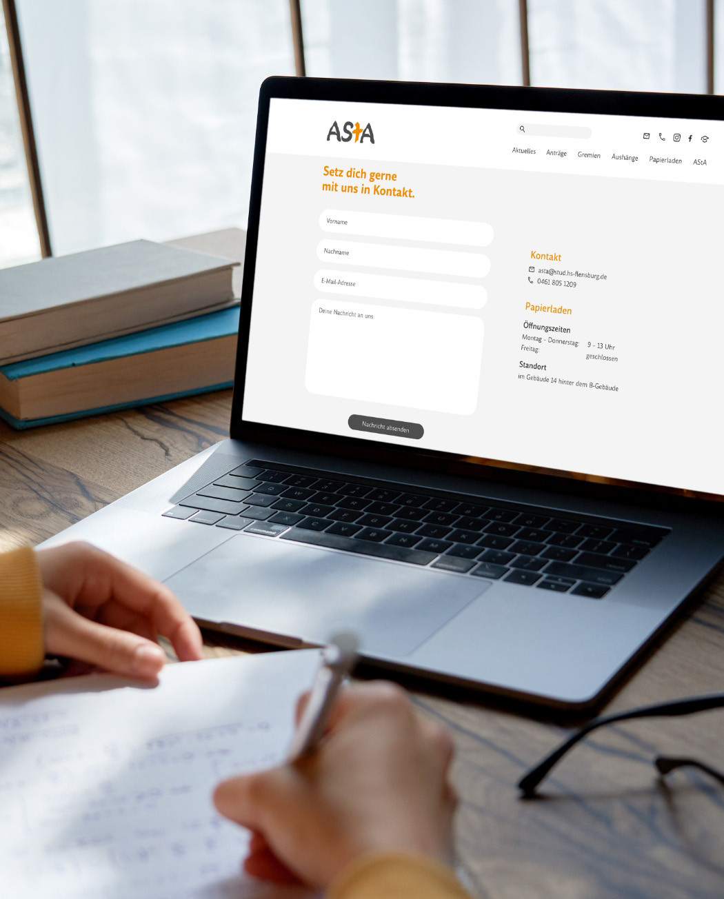 h2_Asta_Teaser_10.jpg Einblicke in die neue Website auf Laptop, Hände mit Block und Stift in der Hand in der Bildecke