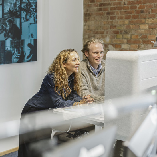 Ein Mitarbeiter und eine Mitarbeiterin von HOCHZWEI blicken gemeinsam auf einen PC