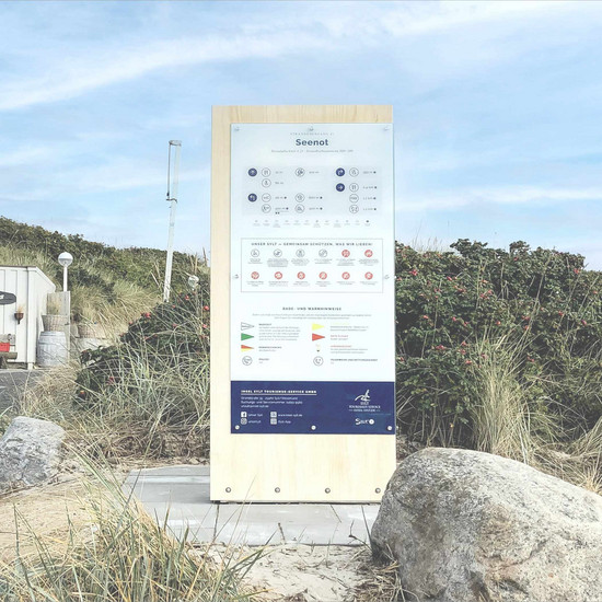Mit den Füßen im Sand Seenot Infotafel steht am Strand von Sylt