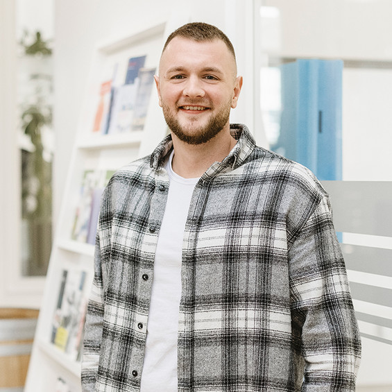 Portrait von Nils-Rasmus Jochimsen. Er lächelt in die Kamera und trägt ein weiß-graues Flanellhemd und ein weißes T-Shirt.