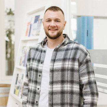 Portrait von Nils-Rasmus Jochimsen. Er lächelt in die Kamera und trägt ein weiß-graues Flanellhemd und ein weißes T-Shirt.