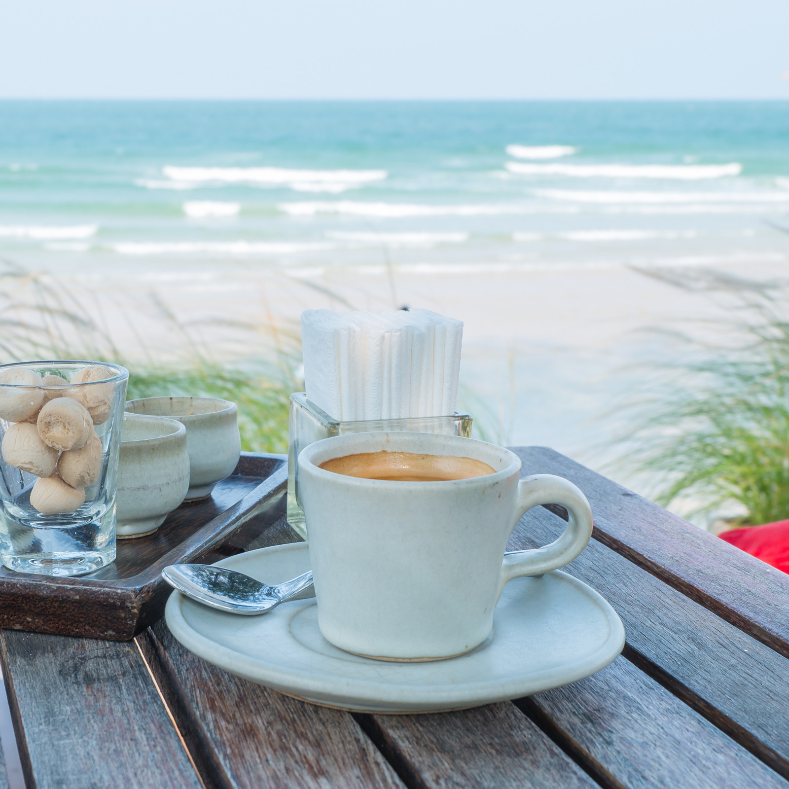 hochzwei_jess_teaser_03.jpg Eine Tasse mit Kaffe steht auf einem Tisch am Meer