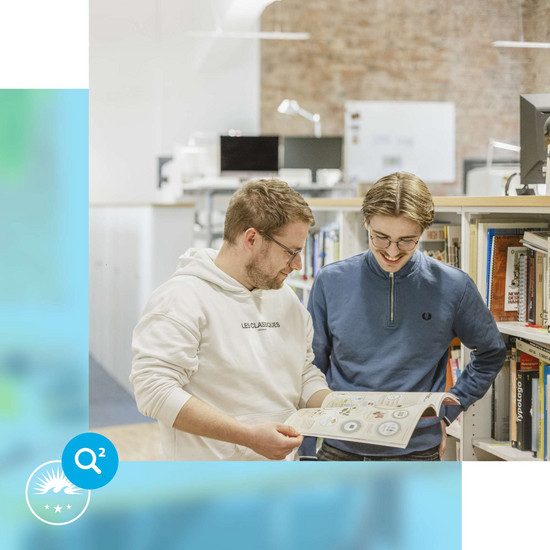 Ausbildung Zwei männliche HOCHZWEI-Mitarbeiter schauen gemeinsam in ein Print-Katalog