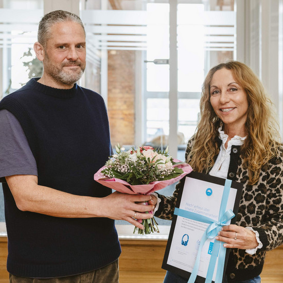 Foto von Timo und Efi. Sie bekommt einen Blumenstrauß und ein Geschenk überreicht. Beide lächeln in die Kamera.