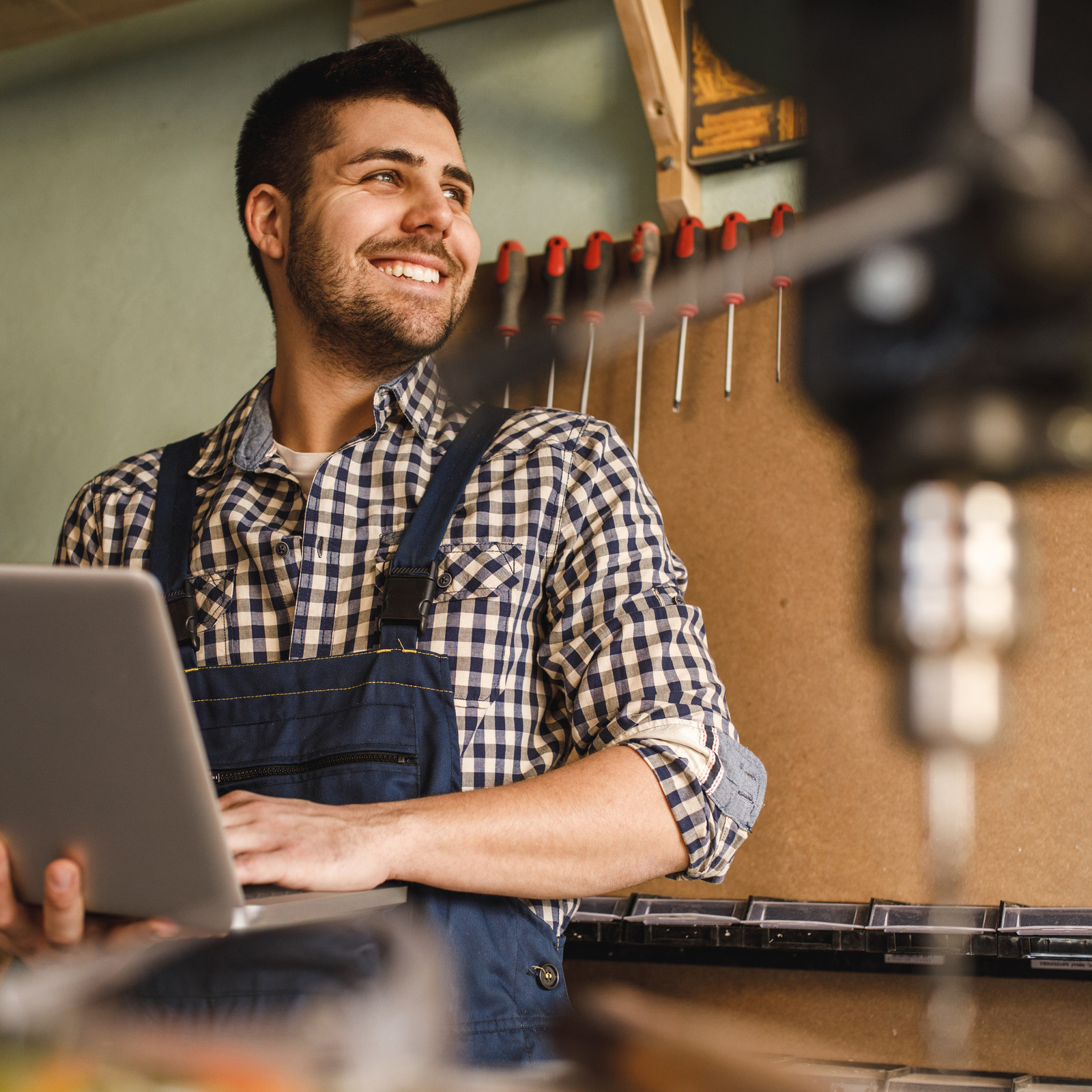 hochzwei_foe_teaser_02.jpg Lächelnder Mann mit Laptop vor Werkzeugwand