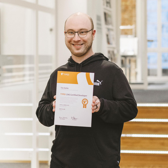 Foto unseres Kollegen Tim. Er hält stolz sein TYPO3 Zertifikat und lächelt in die Kamera.
