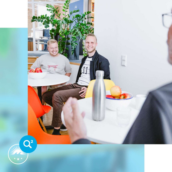 Rastplatz Zwei lachende HOCHZWEI-Mitarbeiter sitzen am Bistrotisch