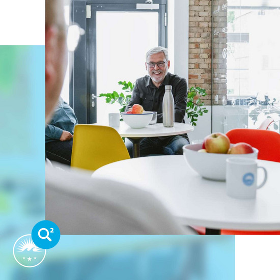 Betriebliche Altersvorsorge Fröhlicher HOCHZWEI-Mitarbeiter sitzt am Bistrotisch