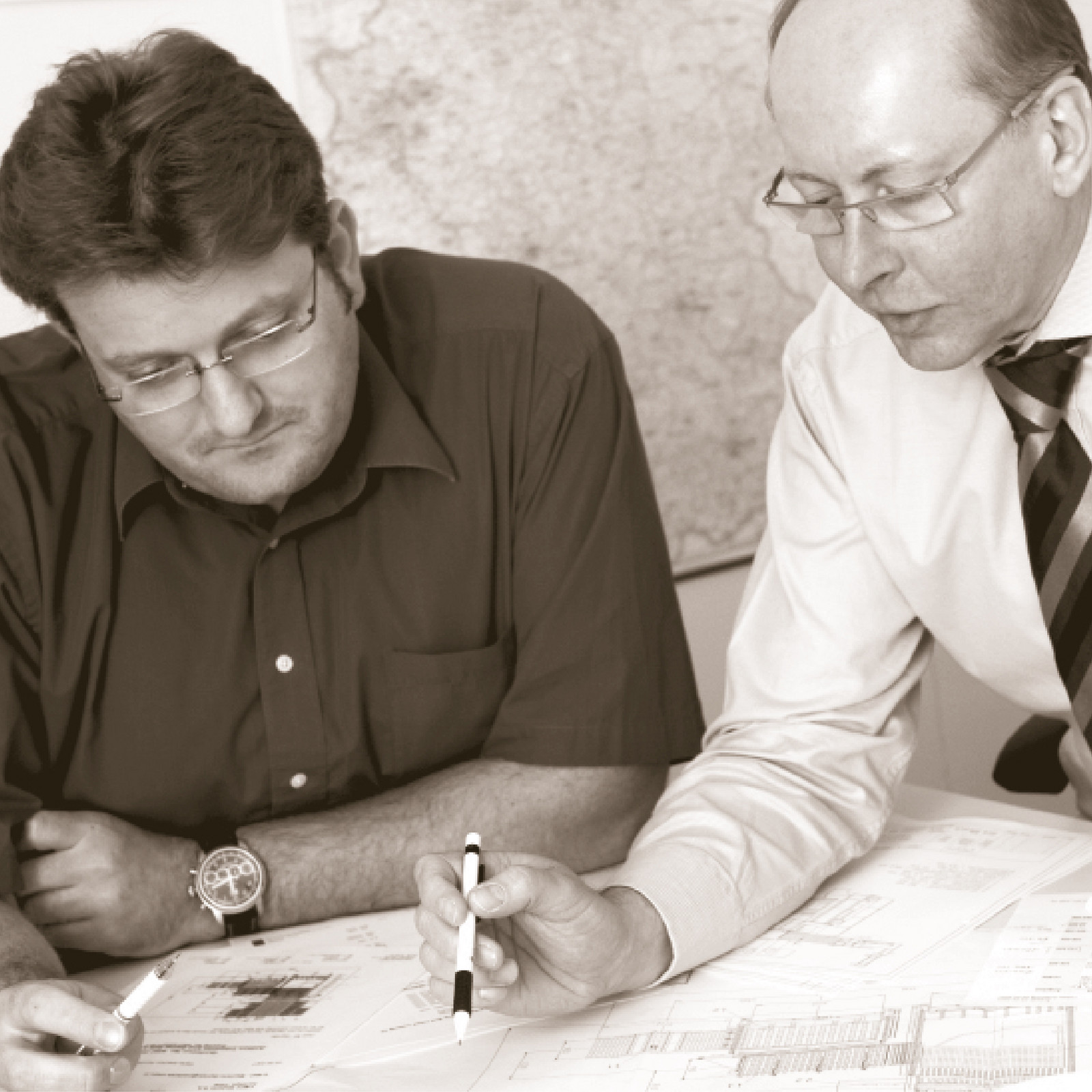 hochzwei_anthon_teaser_03.jpg Zwei Herren schauen auf Pläne, die auf dem Tisch liegen