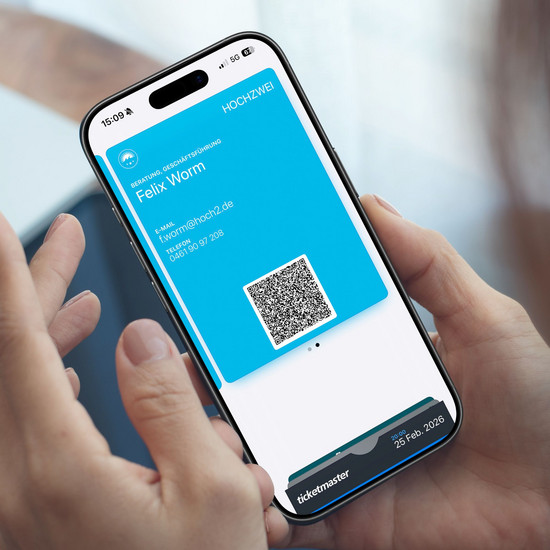 Eine Person hält ein Smartphone mit einer digitalen Visitenkarte mit Name, E-Mail-Adresse, Telefonnummer und einem QR-Code
