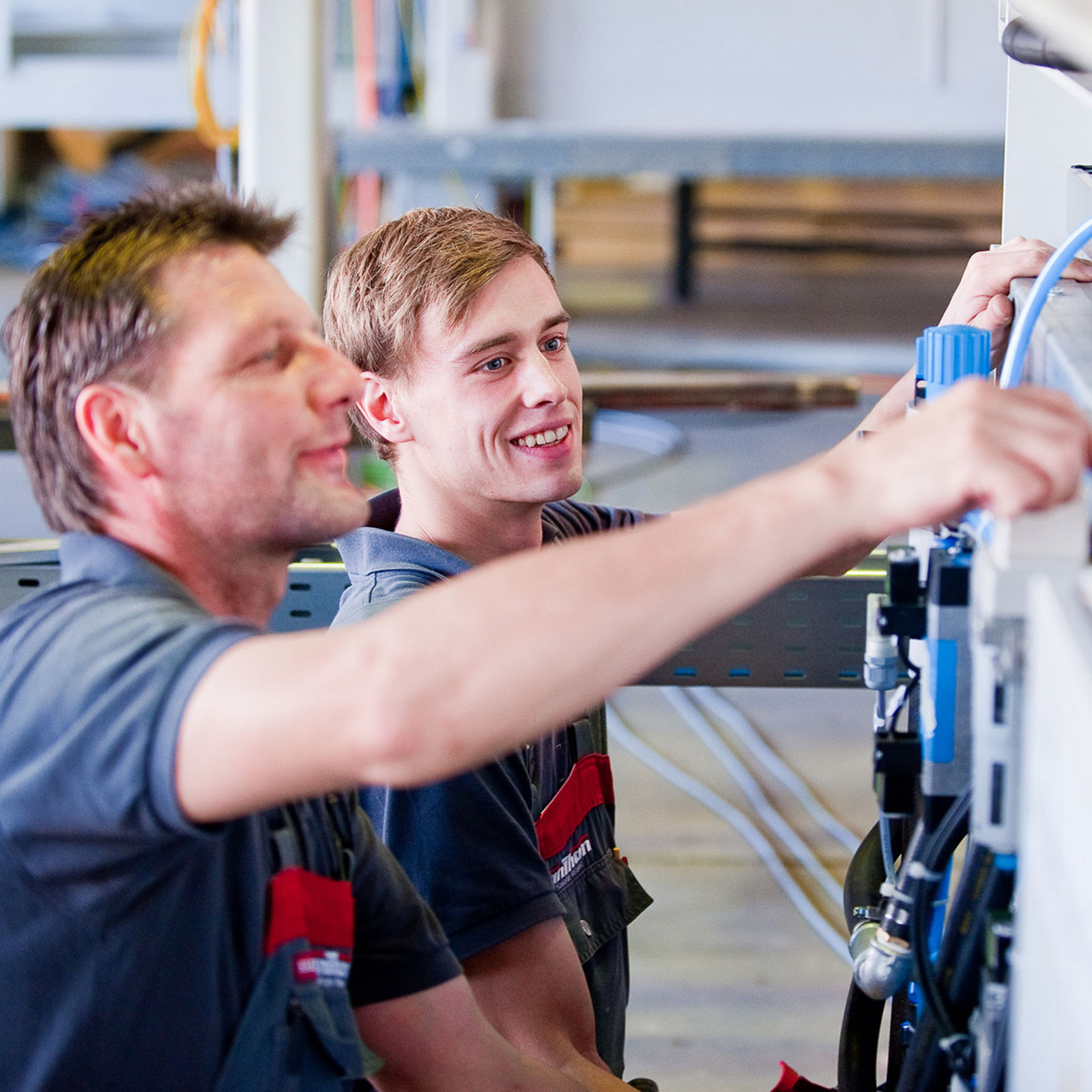 hochzwei_anthon_teaser_03.jpg Ein lachender Mitarbeiter und ein weiterer Mitarbeiter der anthon GmbH an einer Maschine