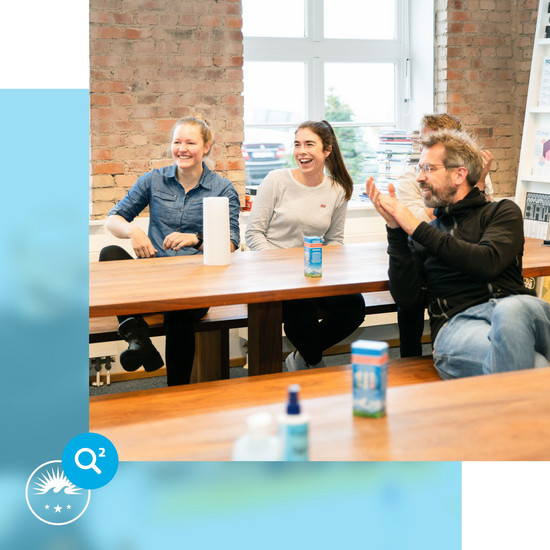 Ohne *** – HOCHZWEI als sicherer Arbeitgeber Vier Hochzwei Mitarbeiter sitzen an einem Tisch