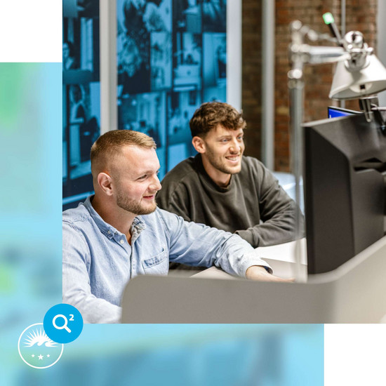 Gleitzeit Zwei männliche HOCHZWEI-Mitarbeiter sitzen lächelnd vor Bildschirmen