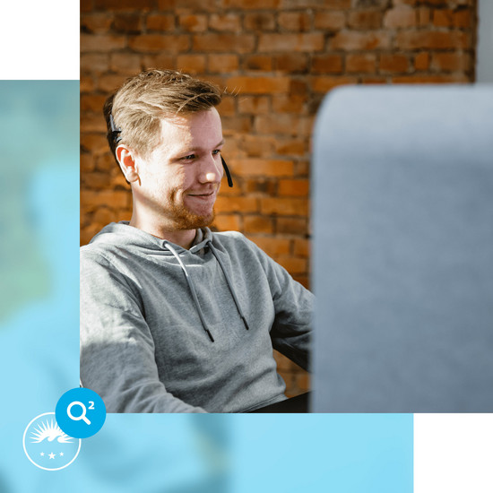 Werkstudenten Junger männlicher Mitarbeiter sitzt mit Headset vor PC