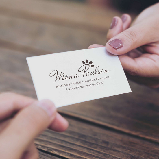 Eine Frau reicht einer Person eine Visitenkarte von Mona Paulsen