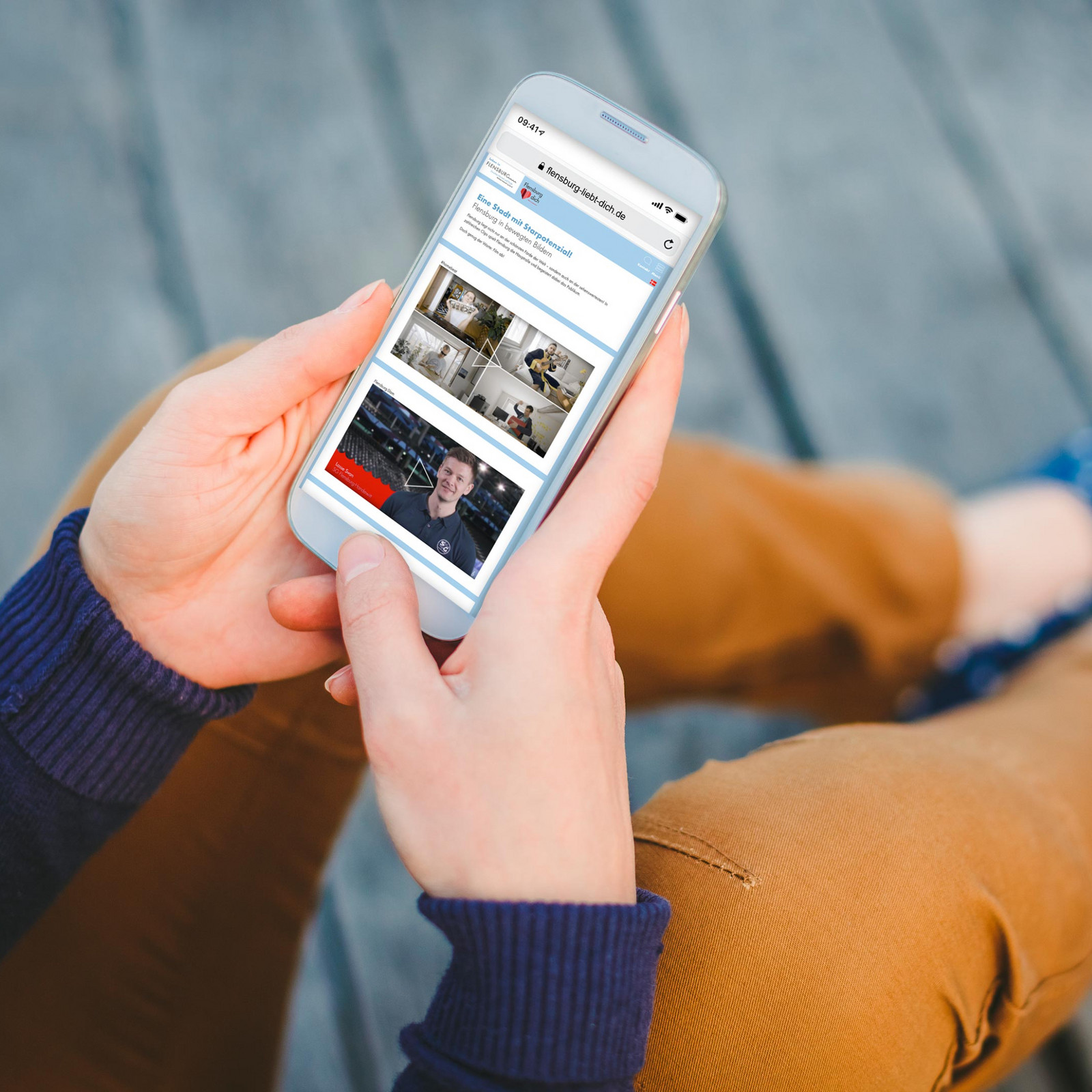 hochzwei_sfdw_teaser_01.jpg Sitzende Person hält Smartphone in den Händen, das die Website flensburg-liebt-dich.de zeigt