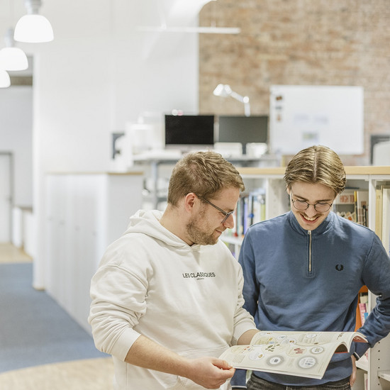 Zwei Mitarbeiter von HOCHZWEI blättern einen Katalog durch