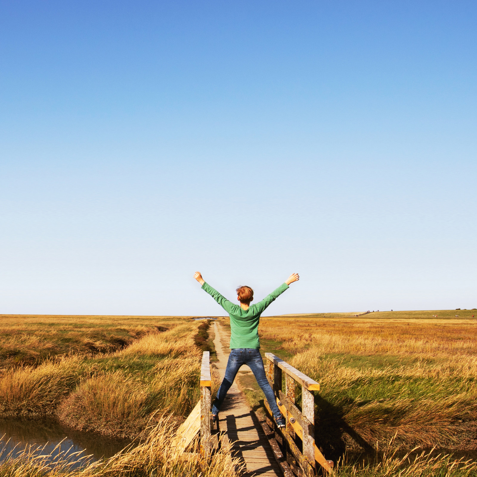 hochzwei_feano_teaser_08.jpg Person mit ausgestreckten Armen auf Prielbrücke in den Salzwiesen