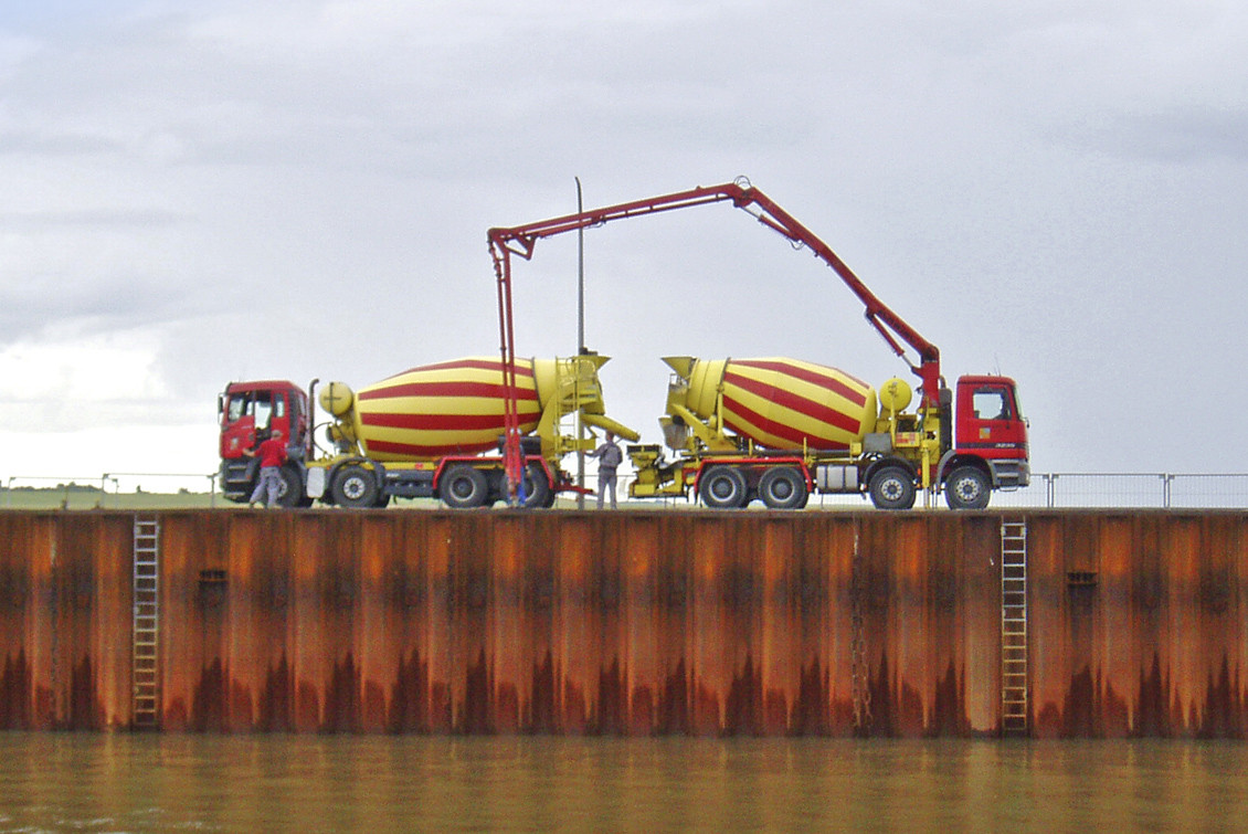 Zwei gelb-rote Betonmischer auf einer Kaimauer