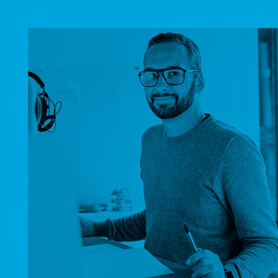 Sie wünschen sich eine neue Website: Was geschieht als Nächstes? Mitarbeiter blickt vom Arbeitsplatz lächelnd in die Kamera