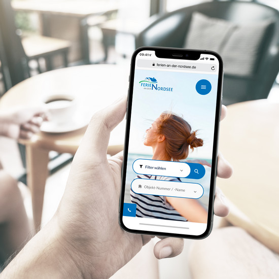 Urlaub am Meer – leicht gemacht. Person hält Smartphone, das Website Ferien an der Nordsee zeigt