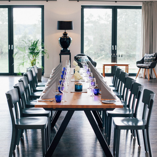 Homepage für Restaurant und Hofladen Mit Weingläsern und grauen Servietten gedeckte lange Tafel mit 12 Stühlen