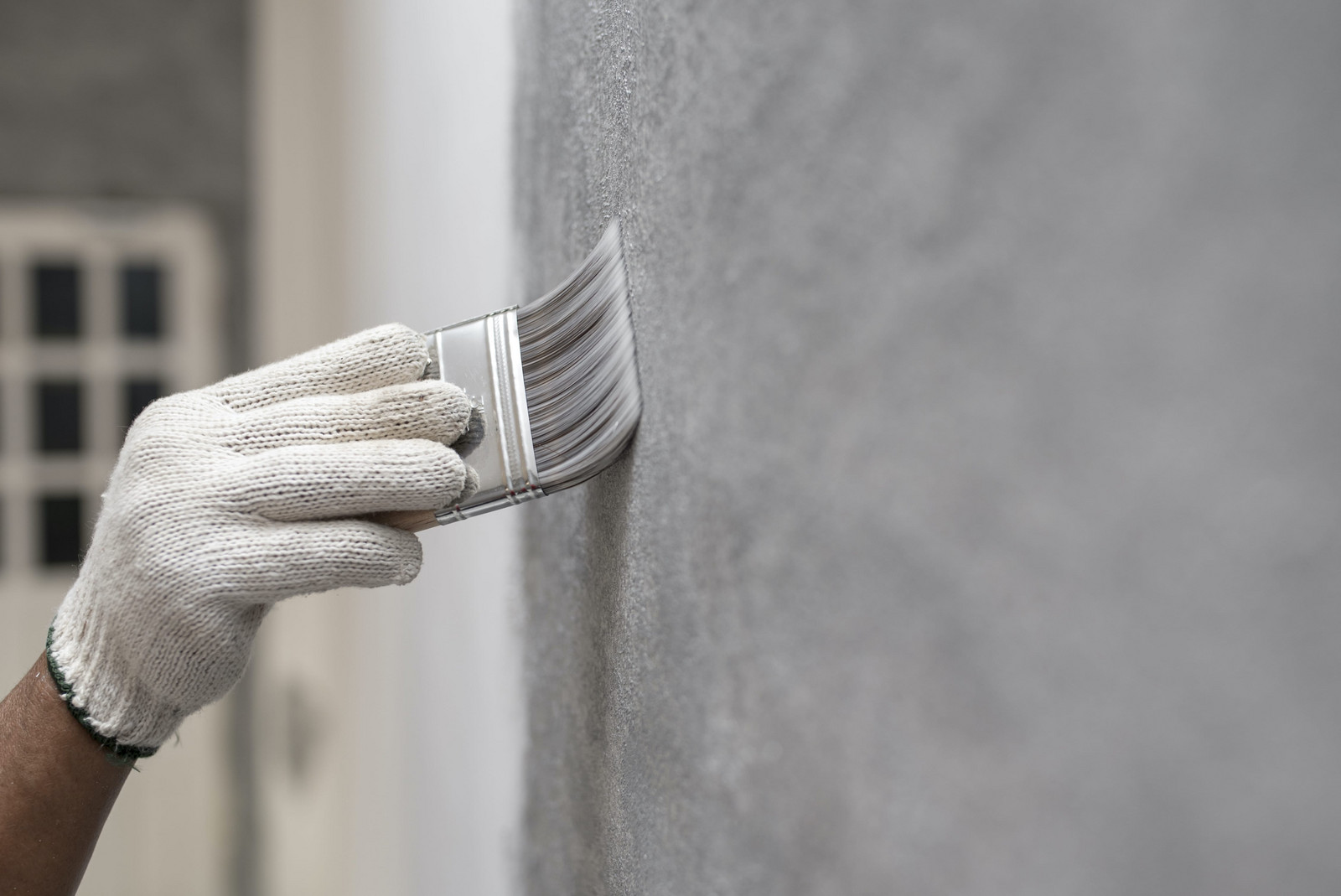 hochzwei_jpj_teaser_gross_01.jpg Ein Mann trägt einen weißen Handschuh während er eine Wand mit einem Pinsel grau streicht