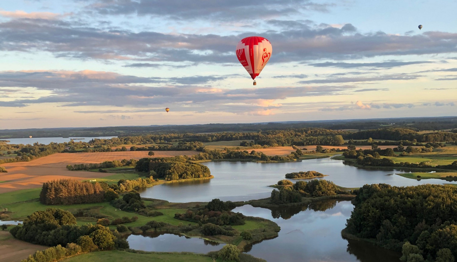 h2_toba_teaser_03.jpg Luftaufnahme einer Seenlandschaft mit einem Heißluftballon